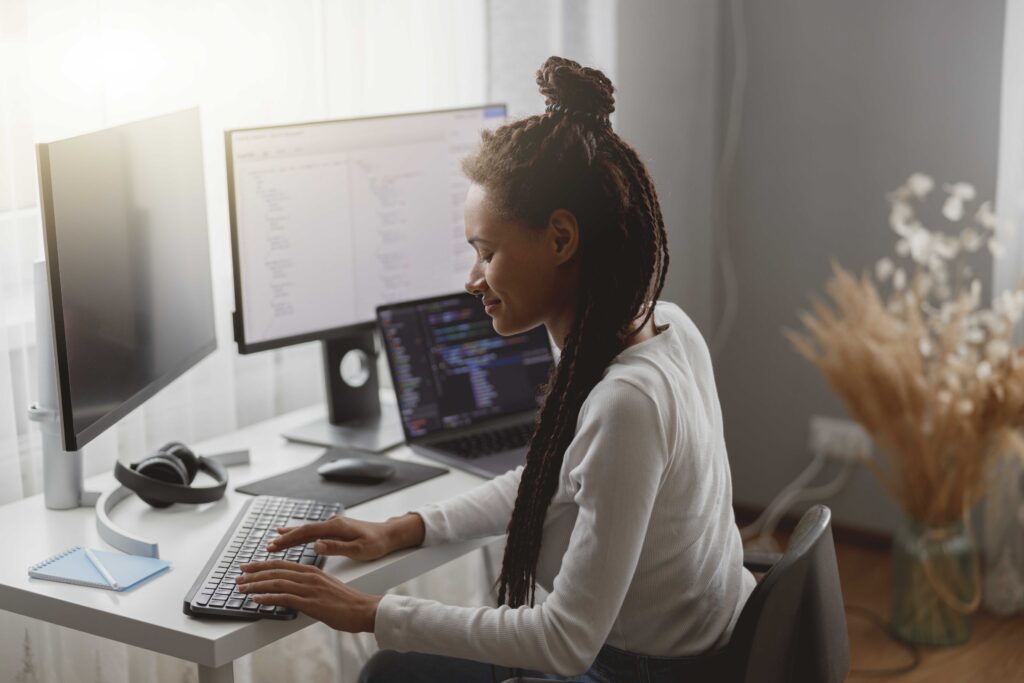 Happy mixed-race woman programmer works in room at home, distance freelance work, coding on computer